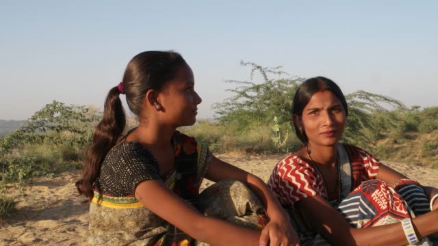 Mano-tiro-estabilizado-de-dos-mujeres-sentado-sobre-una-colina-desierta-arena-en-un-caluroso-día-de-verano-en-la-tradición-India-vestido-sari-mirando-directamente-a-cámara-y-compartir-y-comunicar