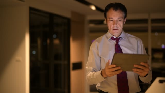 Stressed-Mature-Businessman-In-Office-At-Night-Using-Digital-Tablet-Computer