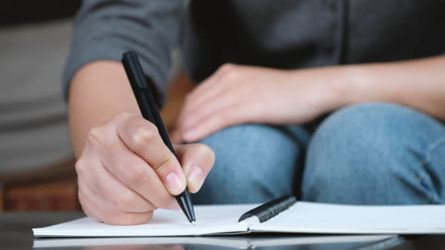 Die-Hand-einer-Frau-auf-einem-weißen-leeren-Notebook-auf-Tabelle-aufschreiben