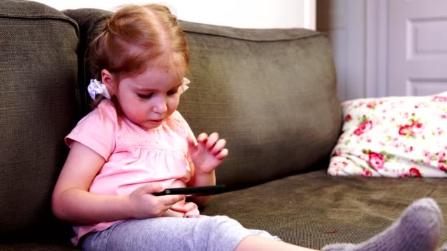 Kleines-Mädchen-mit-einem-Smartphone-zu-spielen-und-in-die-Kamera-schaut