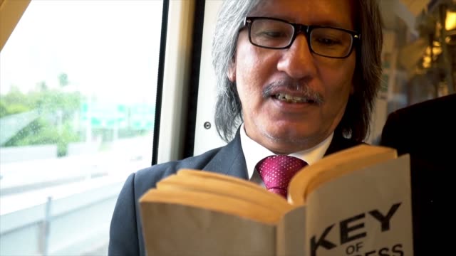 Hombre-de-negocios-Senior-en-gafas-de-lectura-de-un-libro-sobre-las-claves-de-éxito-de-negocios-en-el-tren-con-sonrisa