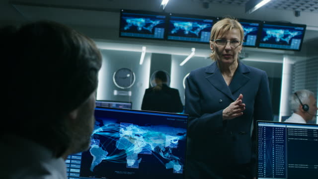 Female-Chief-Operative-Officer-talks-to-Cyber-Security-Dispatchers-Working-on-Personal-Computer-Showing-Traffic-Data-Flow-in-the-System-Control-Room.