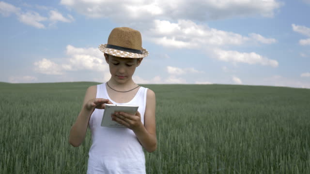 Landwirt-Junge-mit-Hut-verwendet-eine-Tablette-im-Feld,-prüft-die-Ernte