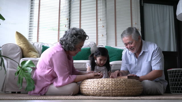 Paar-Senioren-und-Kinder-Mädchen-spielen-puzzle-Spiele-zusammen-im-Wohnzimmer-zu-Hause.-Wachsende-Konzept-der-Kaukasische-Familie,-Bildung,-lernen-und-Entwicklung-des-Alters.-4-k-Auflösung.