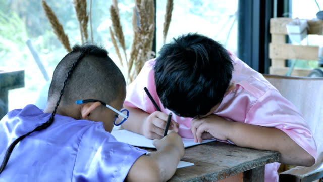 Glücklich-kleine-asiatische-Junge-mit-dem-Schreiben-in-Notebook-und-Bleistifte-zu-Hause.-Bildungskonzept