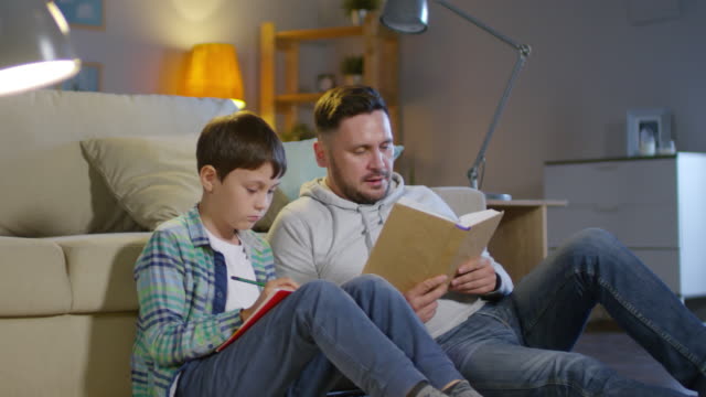 Mann-hilft-Sohn-bei-den-Hausaufgaben-im-gemütlichen-Wohnzimmer