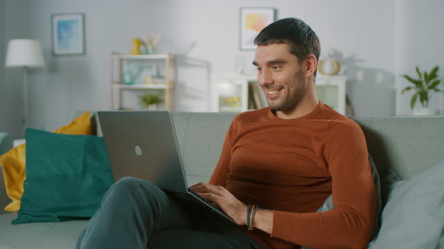 Hübscher-Mann-nutzt-Laptop-Computer-zu-Hause-aufs-Sofa-setzt.-Mann,-arbeiten,-Surfen-über-Internet-aus-seinem-gemütlichen-Wohnzimmer.