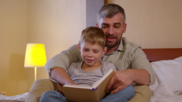 Pequeño-hijo-sonriendo-y-leyendo-cuentos-de-hadas-con-papá