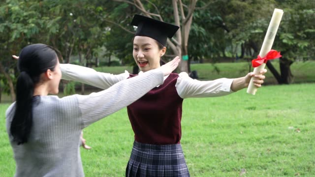 Junge-asiatische-weibliche-Absolventin-umarmt-ihre-Freundin-bei-Abschlussfeier.-Internationale-Vielfalt-Hintergrund