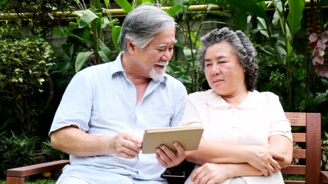 Senior-pareja-sentado-y-usando-tableta-juntos-en-el-jardín-de-casa.