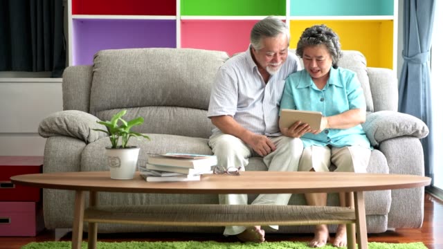 Senior-couple-sitting-and-watching-tablet-in-living-room.