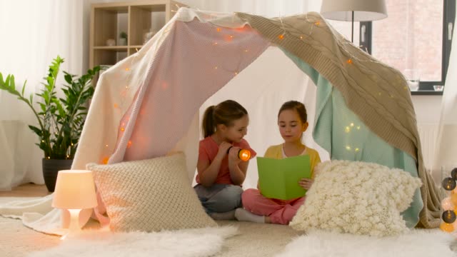 happy-girls-reading-book-in-kids-tent-at-home