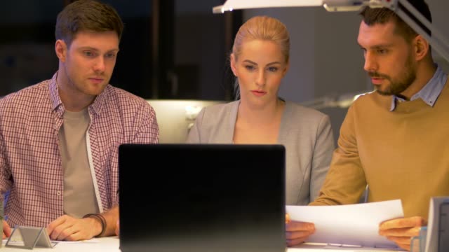 equipo-de-negocios-con-ordenador-portátil-a-trabajar-en-oficina-de-noche