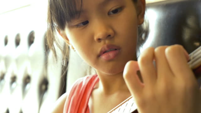 Little-Asian-niño-en-sofá-jugando-ukulele