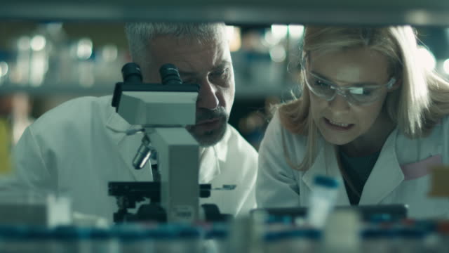 Männliche-und-weibliche-Wissenschaftlerin-arbeiten-mit-einem-Mikroskop-und-einer-Tablette-in-einem-Labor.