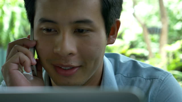 4K:-junge-asiatische-Geschäftsmann-mit-einem-Laptop-während-des-Gesprächs-auf-dem-Handy