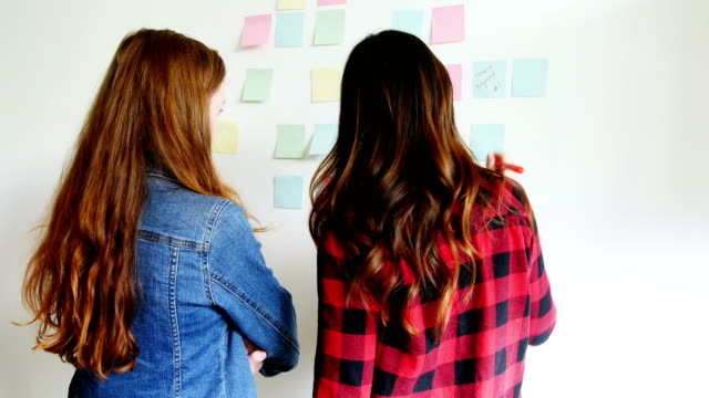 Rear-view-of-female-executives-writing-on-sticky-notes