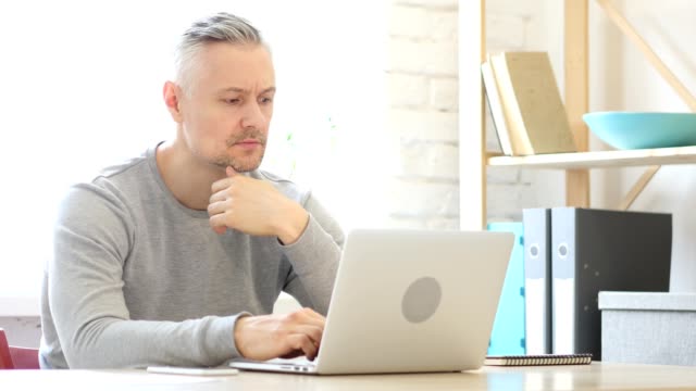 Medio-de-años-hombre-pensando-y-trabajando-en-ordenador-portátil