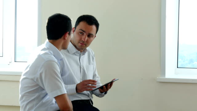 Zwei-Geschäftsleute-sitzen-in-einer-hellen-Büroräume,-auf-der-Suche-nach-Informationen-zusammen-durch-den-Austausch-der-Bildschirm-eines-digitalen-tablet