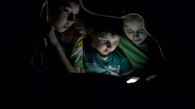 Niños-jugando-en-la-tableta-debajo-de-las-cobijas