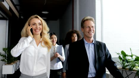 Businesswoman-Make-Phone-Call-Walking-With-Happy-Smiling-Business-People-Team-In-Modern-Creative-Office