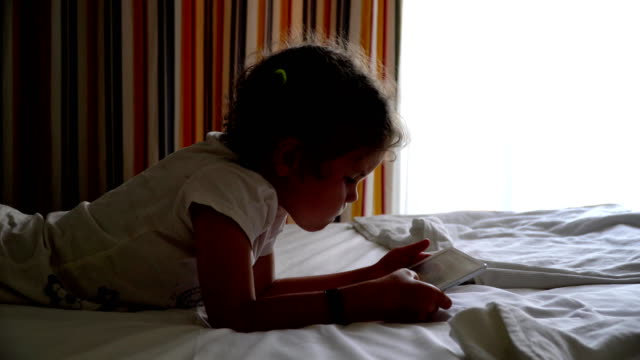 Kleines-Mädchen-spielt-auf-dem-Bett-in-der-Tablette.