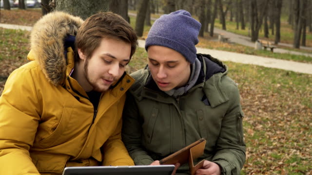 Two-friends-students-uses-laptop-and-tablet-outdoors