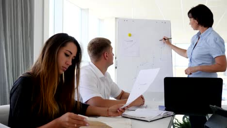 Mentor-in-der-Nähe-von-Diagramm-des-Geschäfts-Entwicklung-über-Whiteboard-spricht-mit-jungen-Partner-im-Büro
