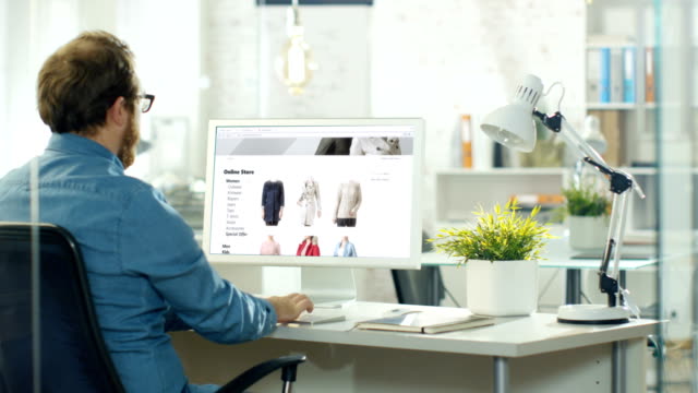 Talentierte-Web-Designer-verwendet-Personalcomputer,-Website-für-Online-Shop-verkaufen-modische-Kleidung-zu-schaffen.-Er-arbeitet-in-einem-modernen-kreativen-Atelier.