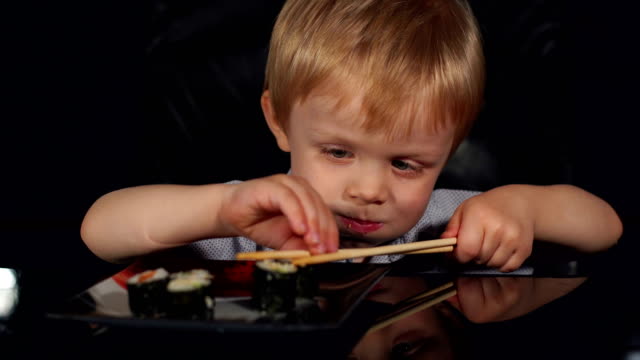 Niño-lindo-comer-sushi-con-palillos-de-madera.