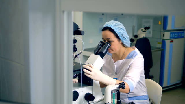 A-woman-in-scrubs-uses-one-of-laboratory-microscopes.