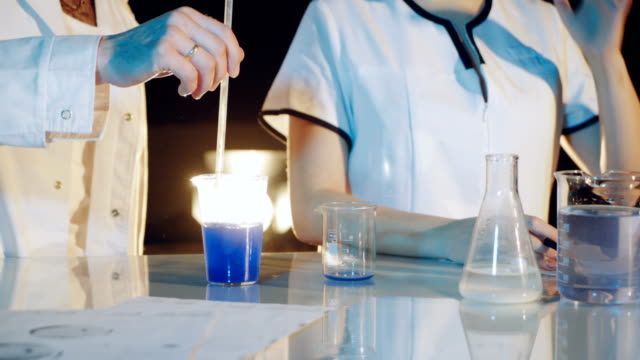 Professionelle-Chemiker-in-einem-Laborkittel-wird-durch-das-Mischen-von-flüssiger-Chemikalien-in-Korbflaschen-experimentiert.