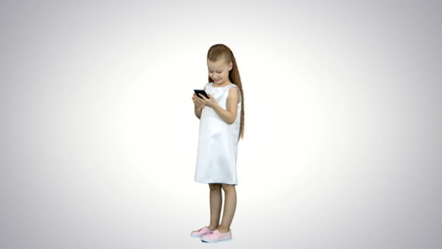 Niedliche-kleine-Mädchen-lächelnd-und-nutzt-ein-Handy-auf-weißem-Hintergrund