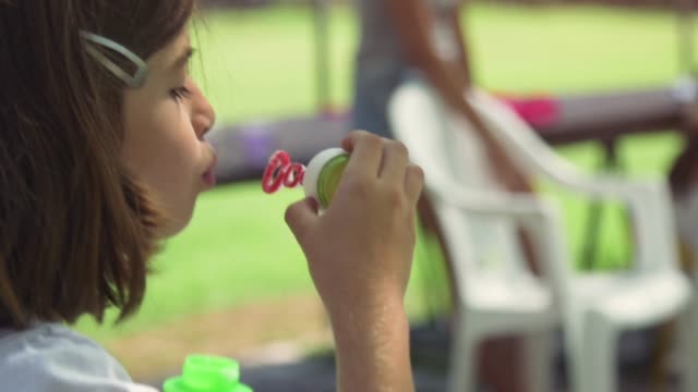 Young-little-girl-using-bubble-blower-outside-at-summer-camp-in-green-field-slow-motion