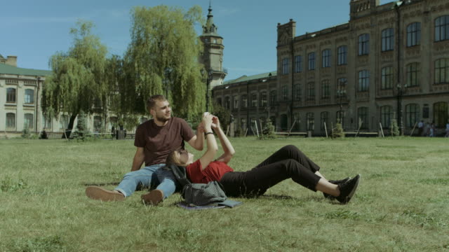Couple-of-students-using-cellphone-on-campus-lawn