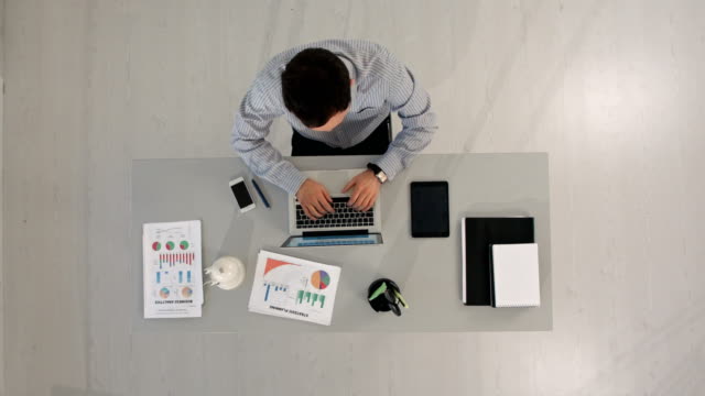 Hombre-trabajando-en-su-computadora-portátil-escribiendo-en-computadora-sentado-en-la-mesa.-Vista-superior