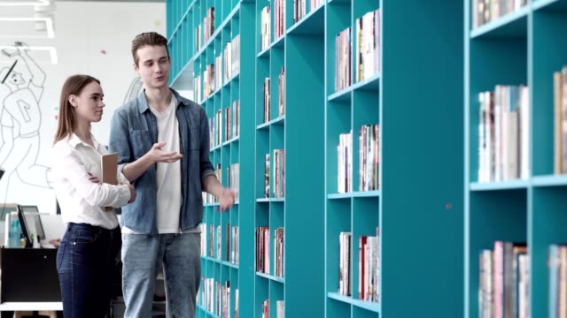 Young-man-and-woman-standing-by-shelevs-in-library-and-choosing-books.-Man-telling-about-his-favorite-books-to-girlfriend