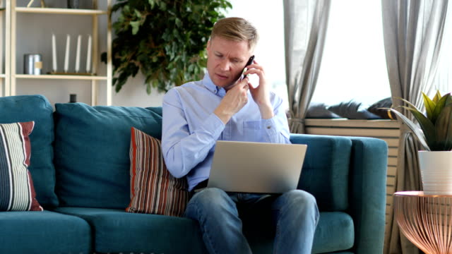 Middle-Aged-Man-Talking-on-Phone-and-Working-on-Laptop