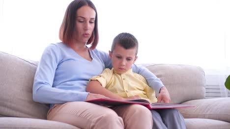 La-madre-sentada-en-el-sofá-y-leer-el-libro-con-el-hijo