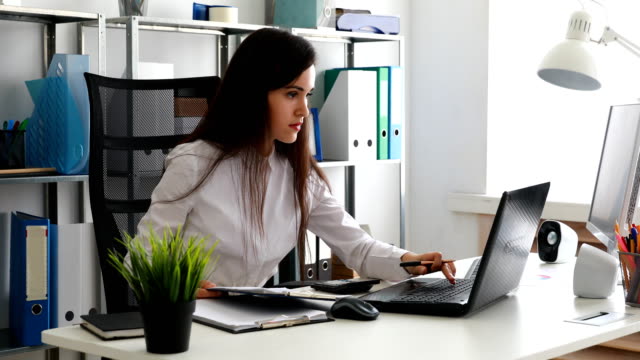 mujer-de-negocios-trabajando-en-ordenador-portátil-y-la-escritura-en-papel-en-la-oficina-moderna