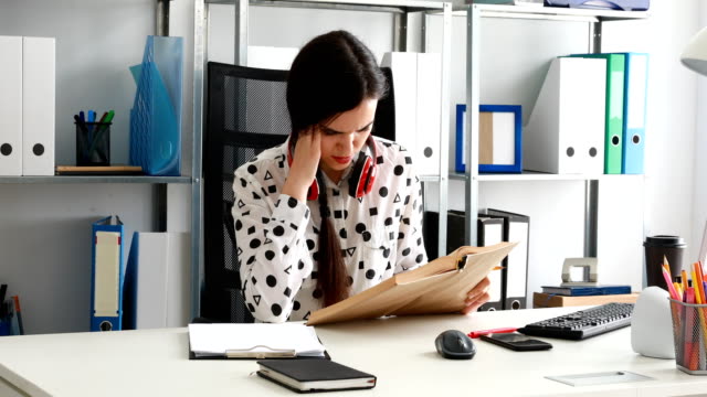 Frau-mit-roten-Kopfhörer-auf-Schultern-schreiben-mit-Bleistift-auf-Papier-im-modernen-Büro