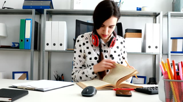 Frau-mit-roten-Kopfhörer-auf-Schultern-Buch-blätterte-und-schreiben-mit-Bleistift-auf-Papier