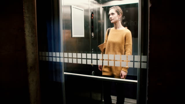 Young-confident-European-woman-pushes-elevator-button,-door-closes-and-she-rides-down,-view-through-a-glass-wall