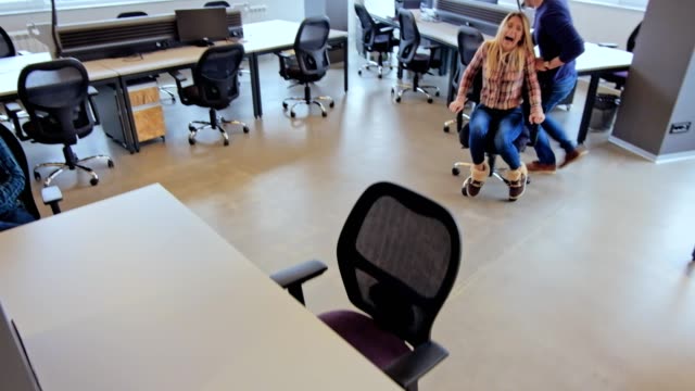 Colleagues-driving-office-chair-through-office