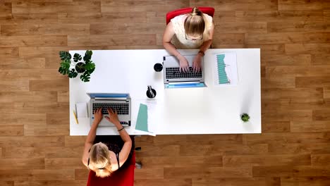 Top-down-Schuss,-zwei-hart-arbeitende-Frauen-Typying-auf-ihren-Laptops-und-sitzen-am-Tisch-im-hölzernen-studio