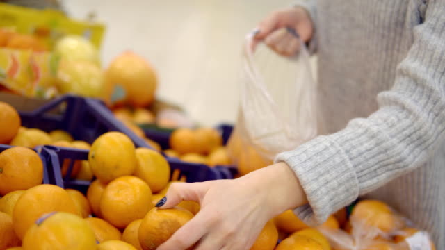 Junge-Frau-in-der-Gemüseabteilung-des-Supermarktes-wählt-einen-Beutel-mit-Mandarinen