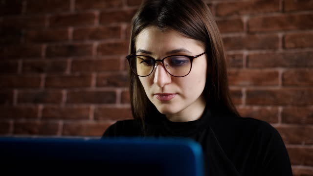 Chica-joven-con-gafas-está-escribiendo-texto-en-el-teclado-del-ordenador-portátil-en-la-oficina.-Joven-periodista-escribe-sobre-el-artículo-de-teclado-del-ordenador-portátil-en-la-edición-en-Internet.