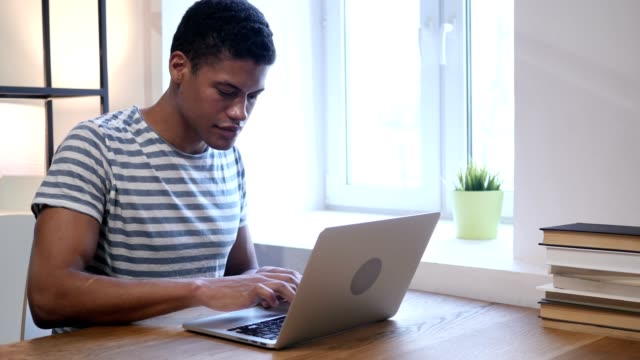 Schwarzer-Mann-feiert-Erfolg-während-der-Arbeit-am-Laptop