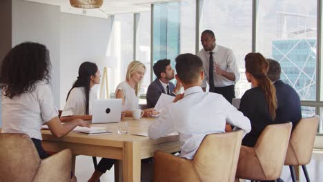 Businessman-Stands-To-Address-Meeting-Around-Board-Table