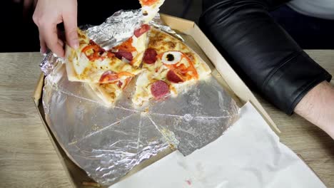 Close-up-Of-People-Hands-Taking-Slices-Pizza-from-food-delivery-open-box.-Tasty-Service-to-office.-Focus-changes-on-hands.-Shot-in-4k